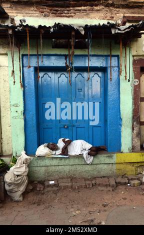 Un Tamil qui fait une sieste par une porte bleue dans le centre de Madurai, Tamil Nadu, en Inde. Banque D'Images