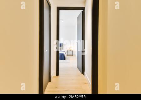 un couloir menant au salon et à la chambre dans un appartement moderne avec parquet clair, murs blancs et finitions noires Banque D'Images