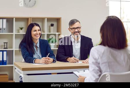 Une femme d'affaires souriante et amicale avec son partenaire d'affaires conduit une entrevue pour une jeune fille brunette en chemise blanche classique. Banque D'Images