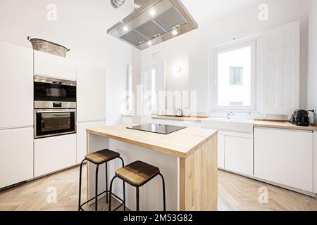 Grande cuisine avec mobilier en bois, mobilier blanc sans poignées, îlot en bois naturel avec hotte et plaque vitrocéramique au centre Banque D'Images