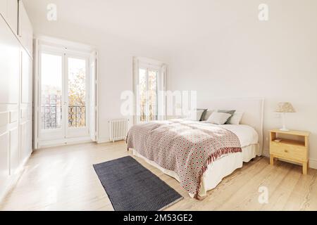 Cette chambre double dispose d''un grand lit, de tables de chevet en bois, de grandes fenêtres avec balcon et d''armoires encastrées blanches Banque D'Images