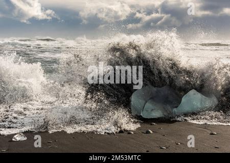 Une onde de tempête qui se transforme en grogners de glace bleue sur le rivage, Diamond Beach, Islande. Banque D'Images