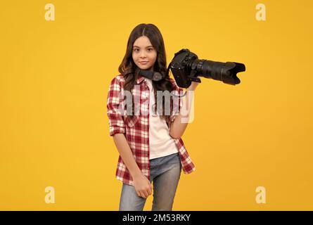 Pleine longueur de jeune fille avec un appareil photo professionnel reflex numérique avec grand objectif photo. Petit photographe isoalté sur fond jaune. École de photo. Banque D'Images