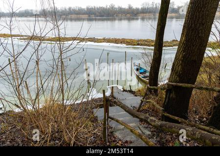 Un vieux bateau de pêche dans un port de pêche abandonné sur une rivière reliée à la glace. Photo prise en hiver, des feuilles de glace près du rivage. Banque D'Images