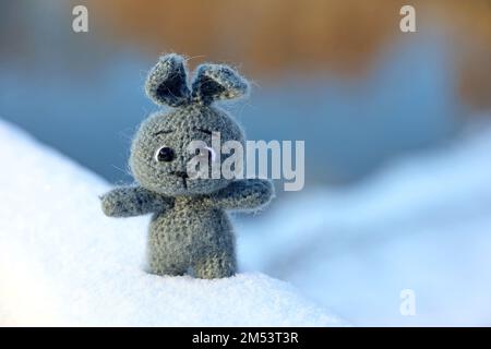 Lapin tricoté gris sur une neige dans un parc d'hiver sur fond flou. Symbole du nouvel an chinois 2023 Banque D'Images