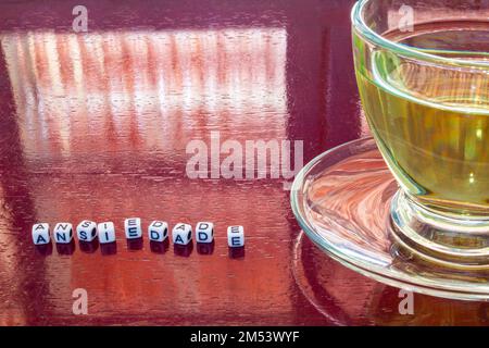 Goiania, Goiás, Brésil – 25 décembre 2022: Détail d'une tasse de thé en verre, sur la table brillante, avec le mot 'anxiété' écrit avec des morceaux. Banque D'Images