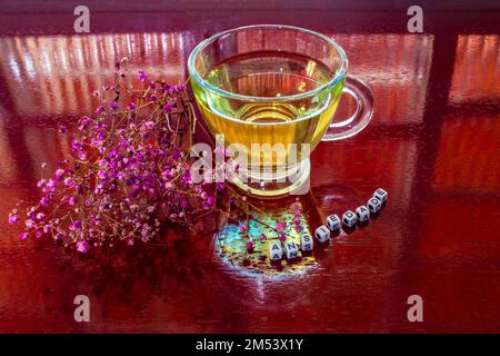 Goiania, Goiás, Brésil – 25 décembre 2022: Une tasse de verre avec thé, sur la table brillante, avec le mot 'anxiété' écrit avec des pièces et des fleurs. Banque D'Images
