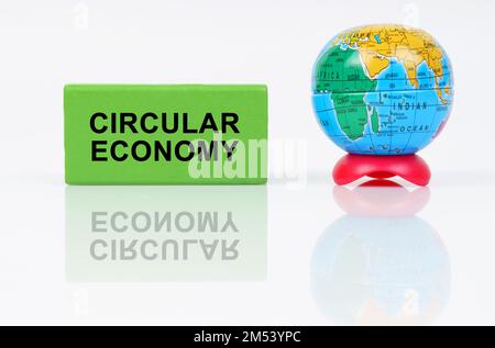 Concept écologique. Sur une surface réfléchissante se trouve un globe et un signe vert avec l'inscription - Circular Economy Banque D'Images