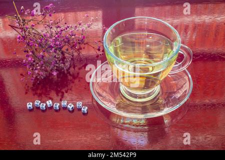 Goiania, Goiás, Brésil – 25 décembre 2022: Une tasse de verre avec thé, sur la table brillante, avec le mot 'anxiété' écrit avec des pièces et des fleurs. Banque D'Images