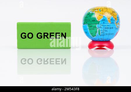 Concept écologique. Sur une surface réfléchissante se trouve un globe et un signe vert avec l'inscription - Go Green Banque D'Images