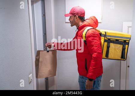 Bon livreur en uniforme rouge avec sac à dos livre un sac de nourriture. Banque D'Images