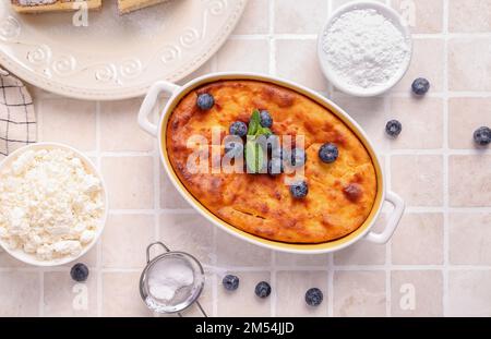 Tarte au fromage délicieuse avec myrtille fraîche sous forme de cuisson et ingrédients sur table en carreaux blancs Banque D'Images