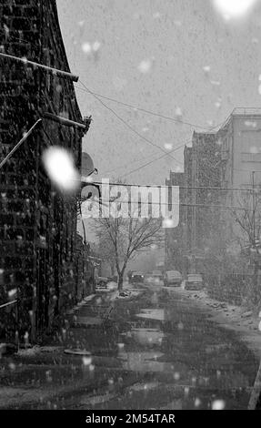 Une rue verticale entre les bâtiments par une journée sombre pendant qu'elle neige en niveaux de gris Banque D'Images