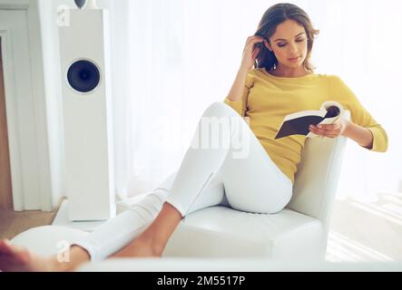Tenir et lire un livre me détend et me revigore. une belle jeune femme se détendant à la maison. Banque D'Images
