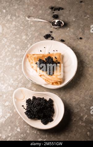 Délicieuse crêpe fine avec caviar noir dans une assiette sur fond métallique Banque D'Images