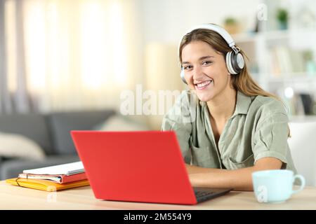 Un bon élève avec un ordinateur portable rouge et un casque vous regarde chez vous Banque D'Images