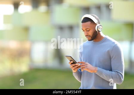 Un homme noir qui marche pour écouter de la musique sur un smartphone dans la rue Banque D'Images