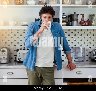 Les week-ends sont pour le café et la contemplation. un bachelor appréciant une tasse de café tout en se relaxant dans sa cuisine à la maison. Banque D'Images