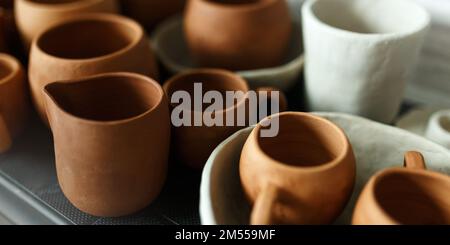 Un gros plan de divers vaisselle en argile séchante sur une étagère. Un concept de studio de poterie. Plats artisanaux, bols, pots, mugs de différentes couleurs. Vue confortable. Banque D'Images