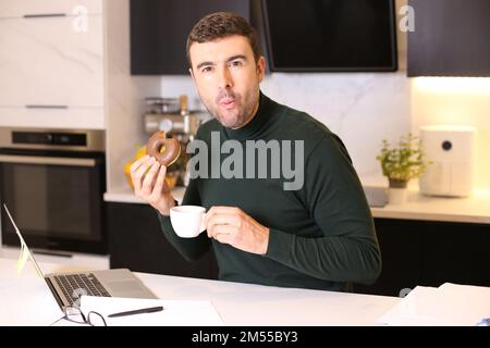 Homme mangeant un beignet et buvant un café au bureau à la maison Banque D'Images