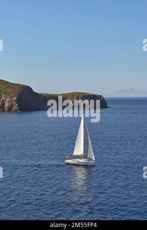 Yacht à voile avec voile blanc sur une mer calme avec la côte en arrière-plan Banque D'Images