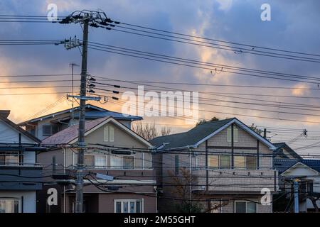 Lignes électriques au-dessus des maisons de banlieue avec nuages de tempête au lever du soleil Banque D'Images