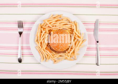 une assiette de hamburger et de frites minimaliste sur une assiette blanche qui repose sur une nappe en coton à rayures entre la fourchette et le couteau Banque D'Images