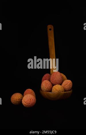 lychees frais dans une cuillère en bois isolée sur fond noir Banque D'Images