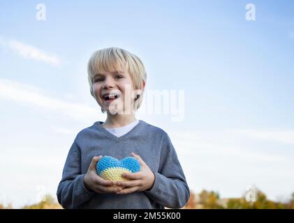 happy boy tient un coeur tricoté jaune-bleu dans ses mains. Les enfants contre la guerre. Croyez en la victoire. Soutenir l'Ukraine, la paix pour les Ukrainiens. Symbole de l Banque D'Images