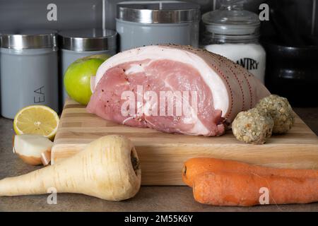 Branche de porc crue non cuite sur une planche à découper en bloc de hêtre avec légumes-racines assaisonnés pour cuire des boulettes de pommes et de sauge et d'oignons Banque D'Images