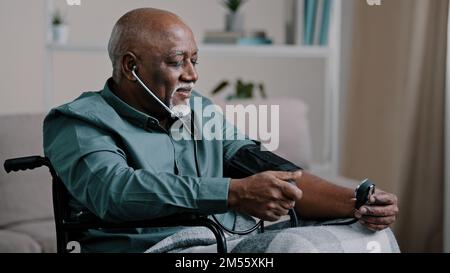 Grand-père âgé africain assis en fauteuil roulant, mesurant une pression artérielle basse élevée, un homme mature à la maison examinant l'hypertension Banque D'Images