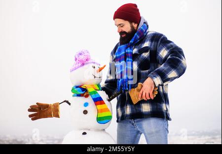 Homme barbu dans des vêtements chauds secoue la main avec bonhomme de neige. Mode hiver. Bonhommes de neige en chapeau, foulard, gants. Banque D'Images