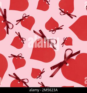 Motif sans couture composé d'étiquettes rouges vides en forme de coeur avec noeud en ruban noué sur fond rose. Concept créatif. Banque D'Images