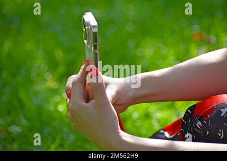 Un gros plan d'une fille prenant une photo avec son iPhone dans un parc avec vernis à ongles rouge Banque D'Images