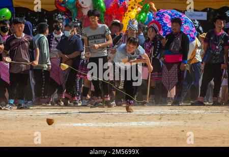 Un homme de tribu de colline de Hmong jouant à la compétition de rotation de haut (jeu traditionnel de tujlub qui implique la rotation de hauts en bois hurlé avec des cordes et des bâtons. Alors qu'un sommet tourne encore, une autre personne essaie du frapper. S'ils ne le frappent pas, ils sont sortis. S'ils le frappent, le gagnant est celui dont le haut continue à tourner le plus longtemps.) Pendant les célébrations du nouvel an de Hmong. En décembre ou janvier, les Hmong célèbrent leur nouvelle année, appelée Noj PEB Caug (prononcé ou PE Chao). Une plus grande célébration publique a lieu dans un lieu en plein air, il y a de nombreuses activités pendant cet événement, comme les TOP-s. Banque D'Images