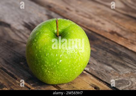Pomme verte avec gouttes d'eau sur fond en bois gros plan. Banque D'Images