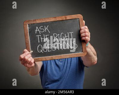 posez les bonnes questions - le texte blanc de craie sur un tableau noir d'ardoise tenu par une personne, l'éducation, la présentation et le concept de communication d'affaires Banque D'Images