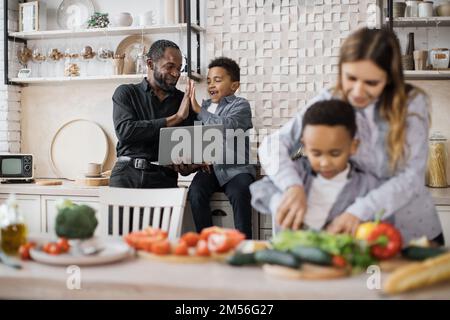 Concentrez-vous sur l'amour du père africain et petit garçon enfant trouver la recette de repas de vacances et de donner haut cinq. Bonne mère enseigner petit fils de préchooler hacher des légumes préparer la salade pour le déjeuner ensemble. Banque D'Images