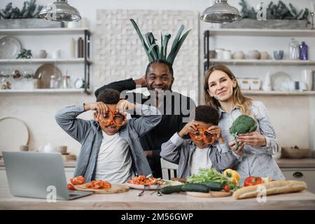 Souriant heureux heureux parents et enfants heureux s'amuser tout en cuisinant dans la cuisine. Drôle de maman, papa et les enfants de faire des verres de tranches de poivre, de couper des légumes pour la salade. Repas de famille à la maison. Banque D'Images