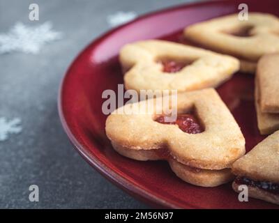 Biscuits de Noël Linzer remplis de marmelade aux fraises rouges sur une assiette rouge. Gros plan. Banque D'Images