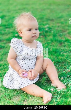 adorable bébé en robe à pois joue avec une poupée dans le parc Banque D'Images