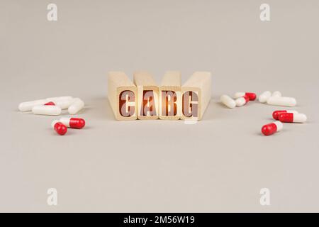Concept médical. Sur une surface grise se trouvent des pilules et un bloc de bois rouge avec l'inscription - CABG Banque D'Images