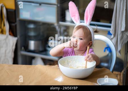 Joyeuses pâques, famille portant des oreilles de lapin serre-tête dans la cuisine et la préparation du gâteau de pâtisserie Pâques ensemble, petite fille aidant sa mère préparer la tarte et Banque D'Images