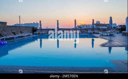 Une piscine typique à Mykonos à côté d'un petit hôtel est l'une des îles grecques au coucher du soleil et l'avion fait un cercle pour atterrir à l'aéroport de Mykonos. Banque D'Images