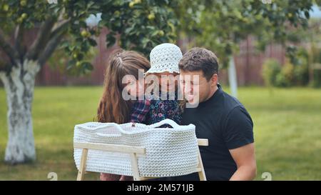 Une jeune famille regarde son nouveau-né dans un berceau dans le jardin. Banque D'Images