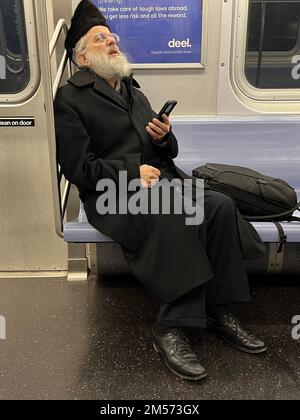 Juif orthodoxe en prière avec son smartphone alors qu'il passe un métro tr4ain à Brooklyn, New York. Banque D'Images