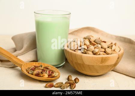 Verre de lait pistache, bol avec noix et cuillère avec grains sur table légère Banque D'Images