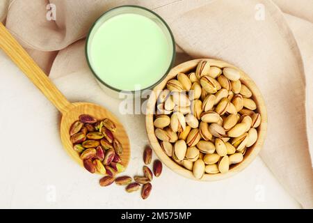 Verre de lait pistache, bol avec noix et cuillère avec grains sur fond clair Banque D'Images