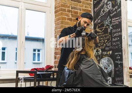 Nouveau concept de coiffure. Spécialiste des cheveux concentré travaillant sur la repousse des cheveux de son client. Intérieur du salon de coiffure. Photo de haute qualité Banque D'Images