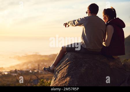 Je peux voir votre maison d'ici. Vue arrière d'un jeune couple en admirant la vue depuis le sommet d'une montagne. Banque D'Images